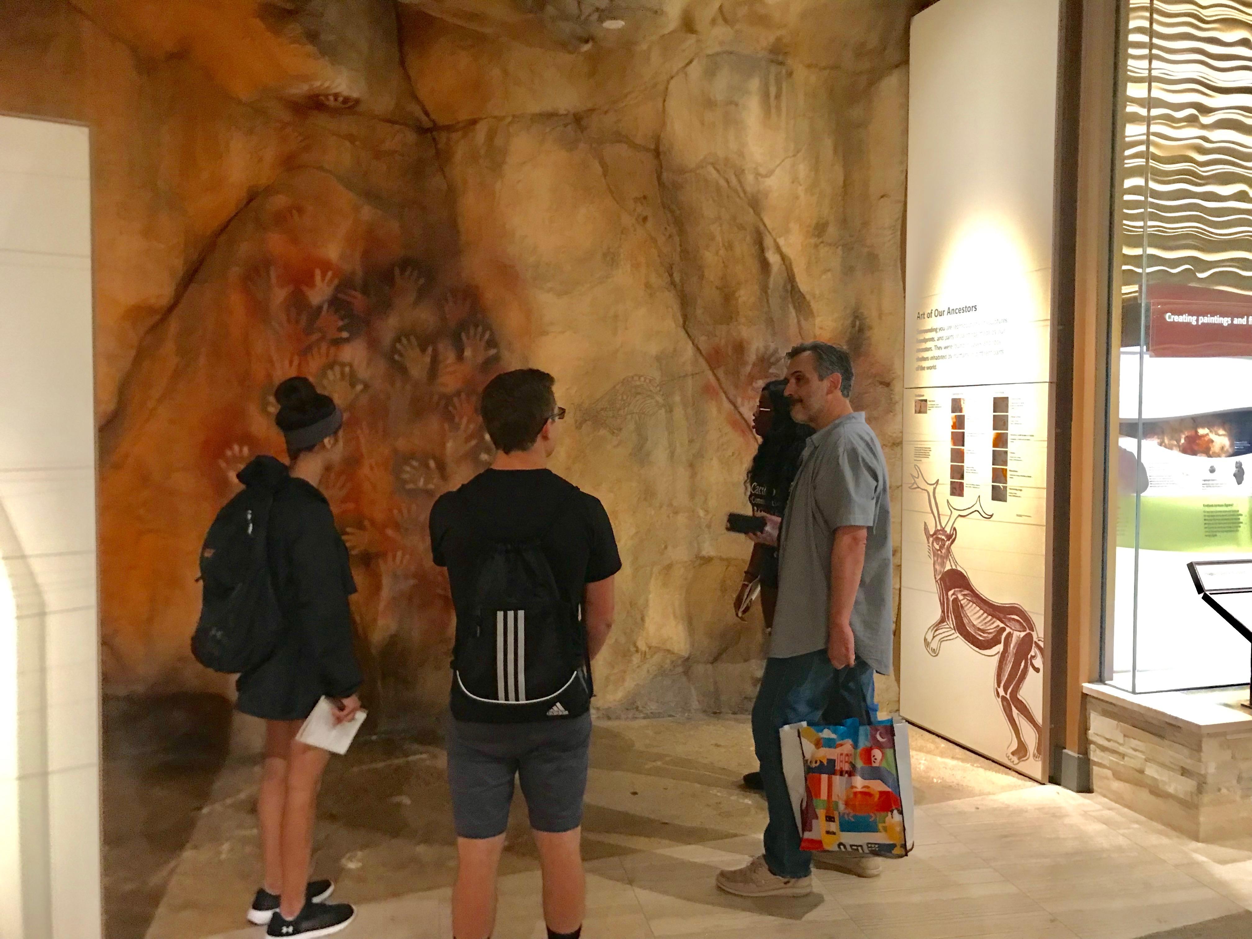 three people stand near cave wall in museum
