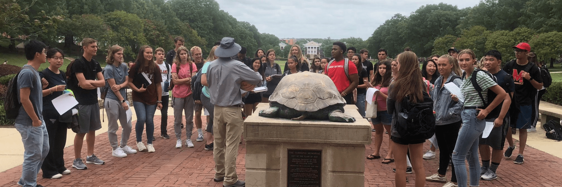 group of students face Testudo statue and professor in safari outfit
