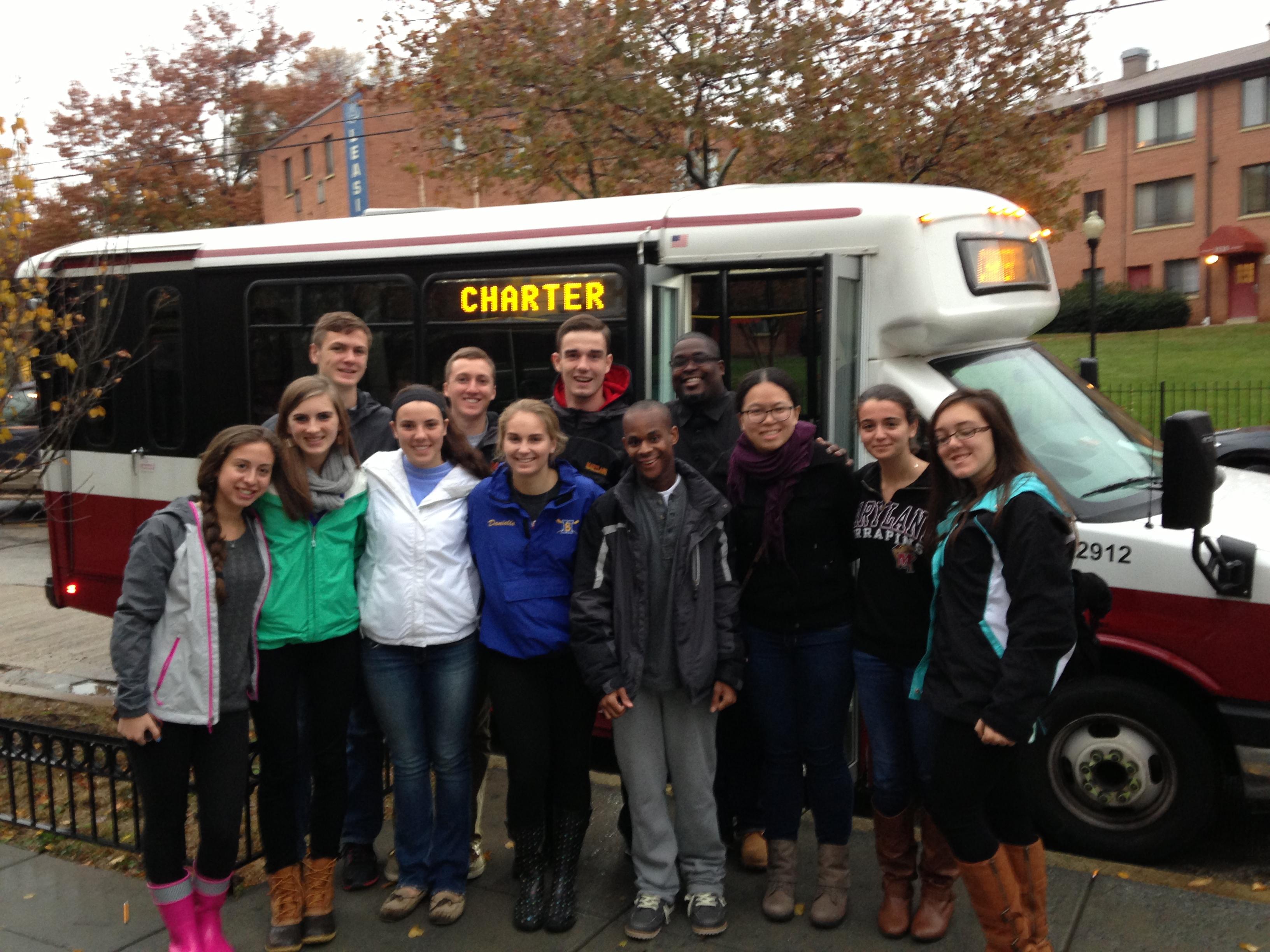 group of students pose in front of shuttle bus